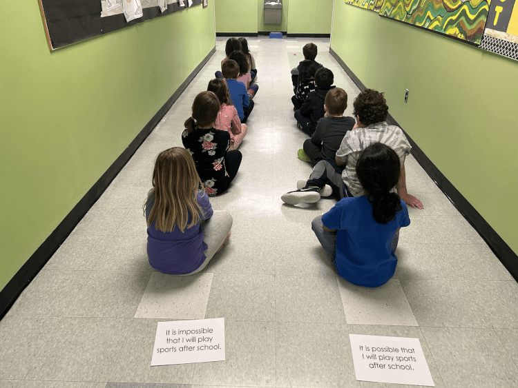 Photo of students sitting on the floor, one behind the other, forming two lines, each represented by a statement.